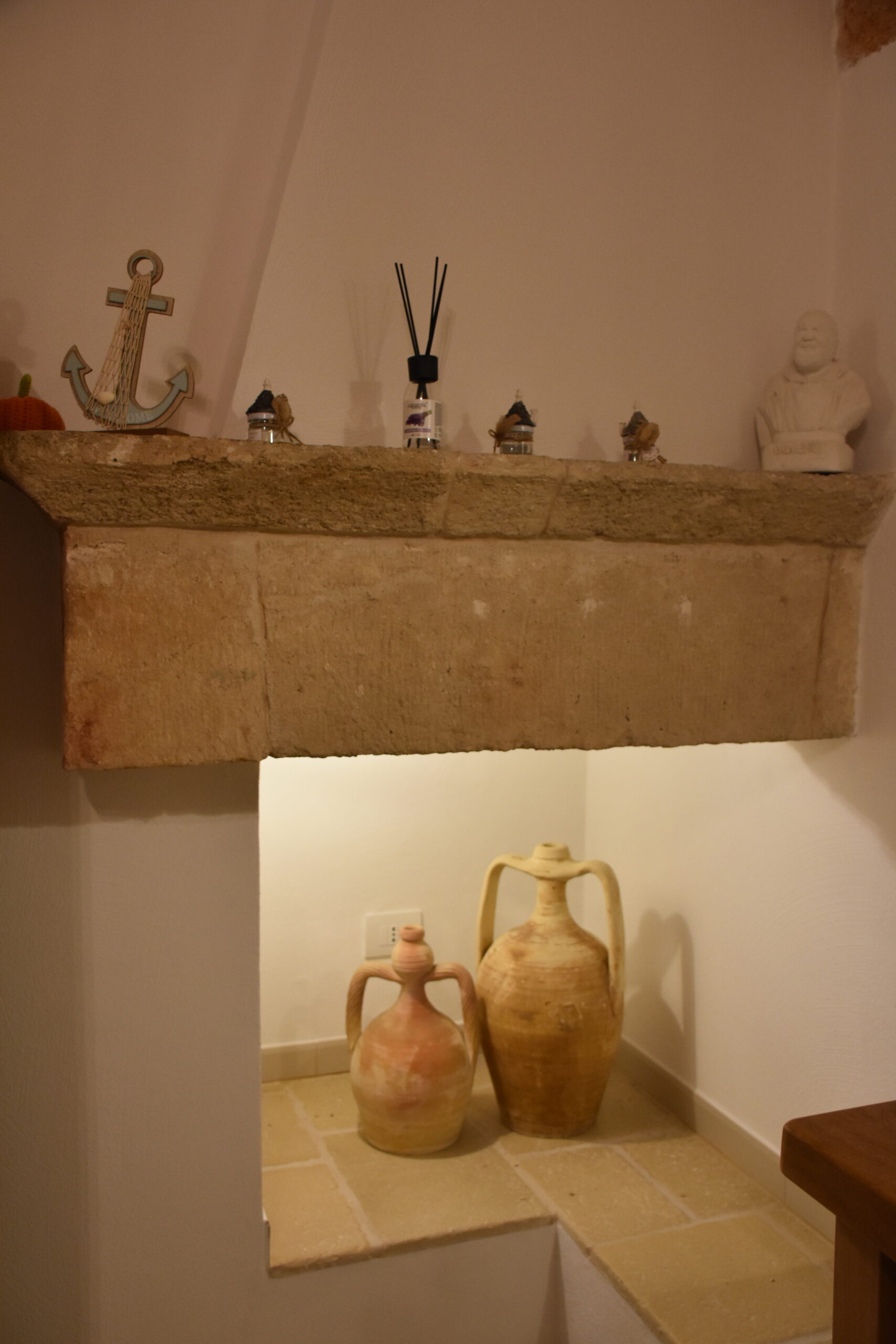 Camino interamente in pietra della suite Perlaura con all'interno due antiche anfore una più grande e una più piccola in terracotta. Sulla parte superiore del camino uno spazio con elementi decorativi tra cui un ancora.