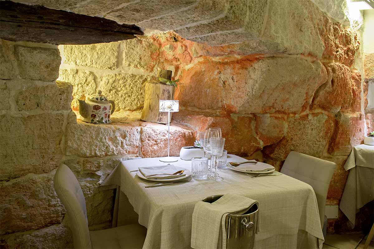 Ristorante romantico in pietra a Polignano a Mare, tavolo elegante apparecchiato per due, atmosfera intima con luce soffusa, nel cuore del centro storico.